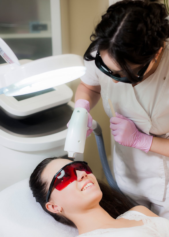 Woman receiving laser hair removal treatment on her face from a technician wearing pink gloves and protective eyewear in a clinical setting
